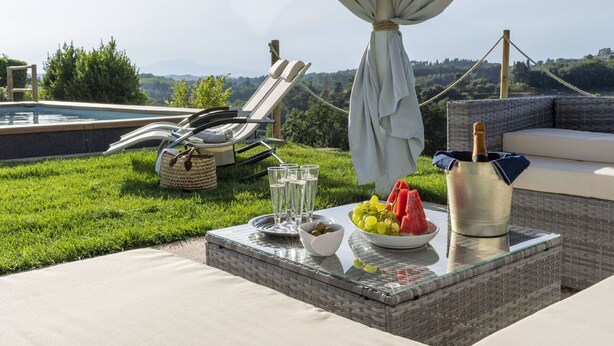 Een terras bij het zwembad met een tafel gedekt voor een maaltijd, inclusief een fles champagne, glazen en een schaal met druiven en watermeloen.