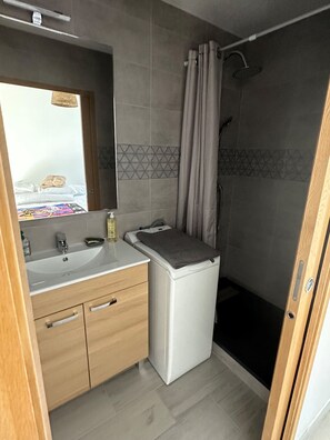 A compact bathroom with a sink, mirror, and shower.