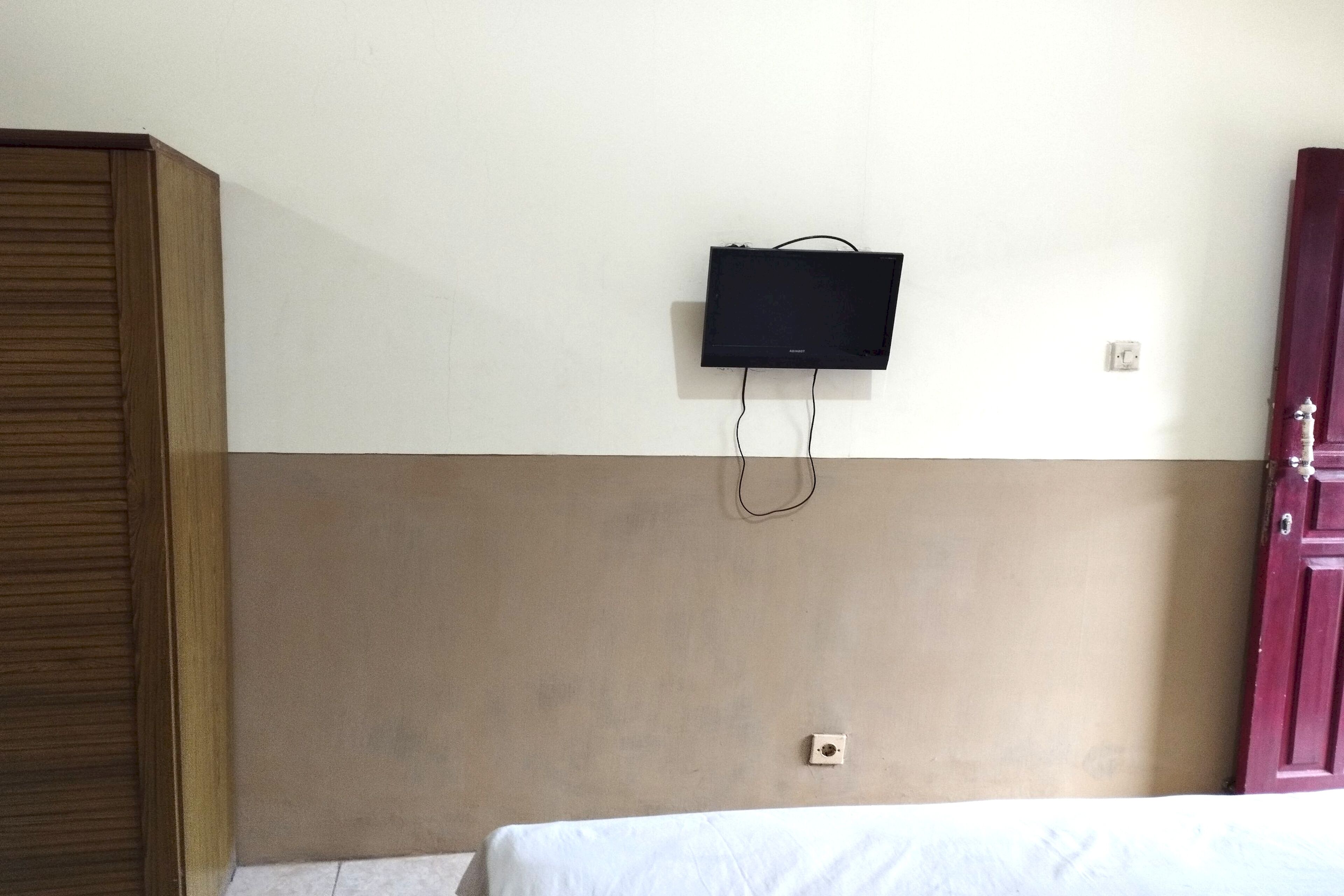 A room with a bed, a television mounted on the wall, and a wooden wardrobe.