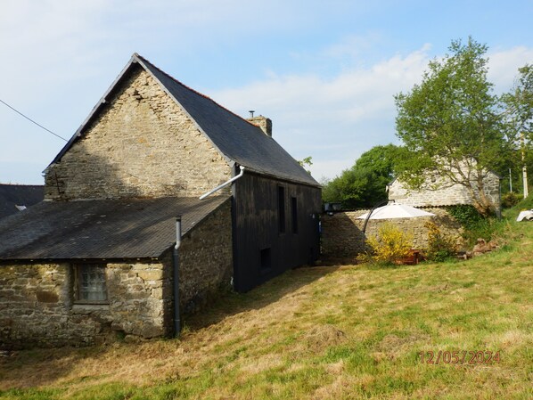A stone building with a sloped roof, a small window, and a grassy area in front.