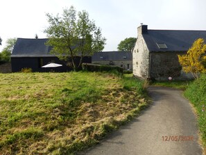 A rural property with a stone building, a paved path, and a grassy field.