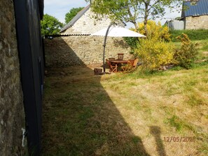A stone building with a tiled roof, a wooden table and chairs, and a white umbrella.