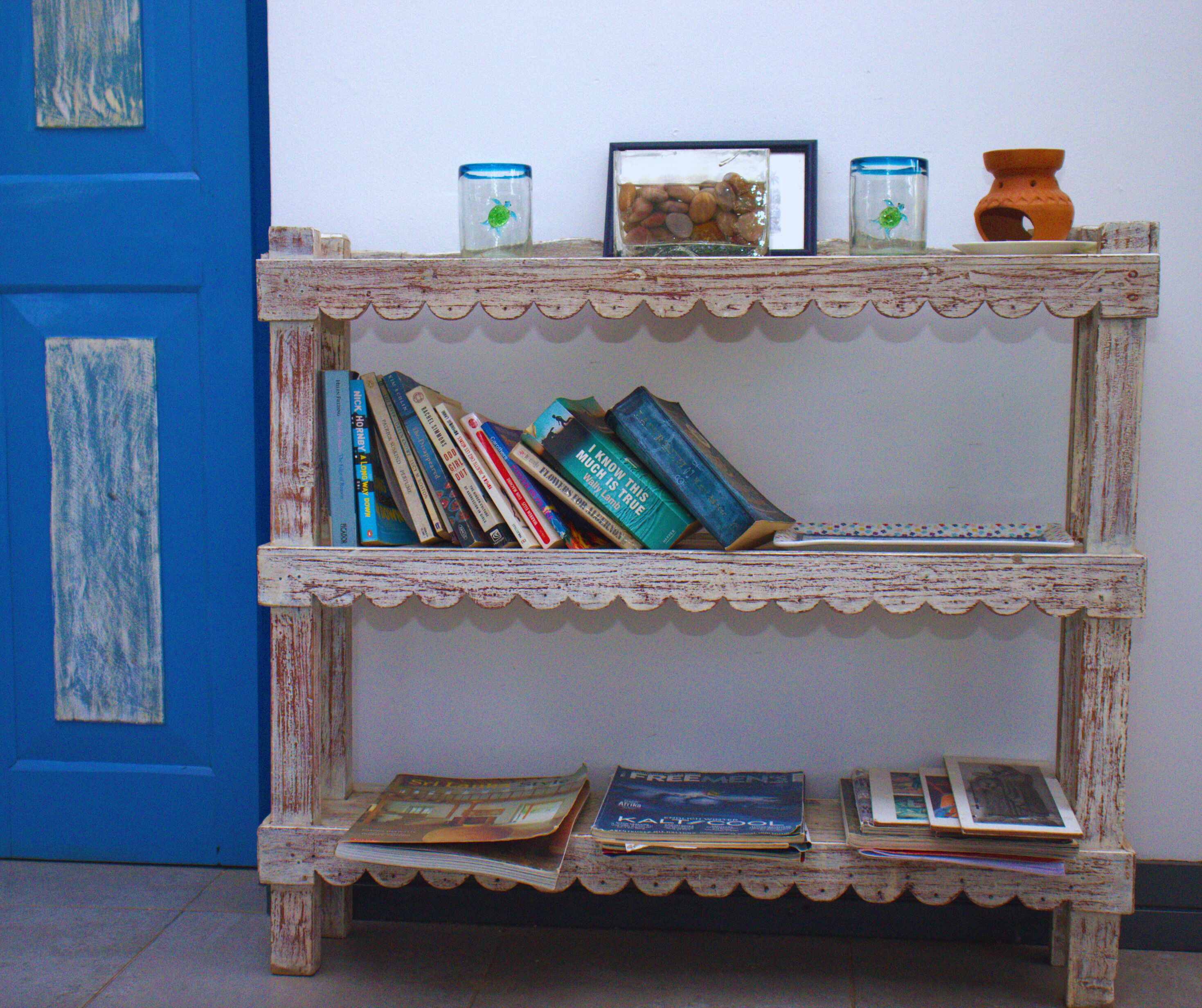 Une bibliothèque en bois rustique, dotée de plusieurs étagères, sur laquelle sont posés quelques livres et des objets décoratifs.