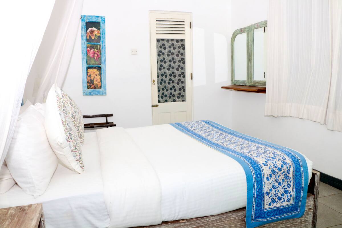 Een slaapkamer met een bed, nachtkastje, spiegel en een deur met raam.