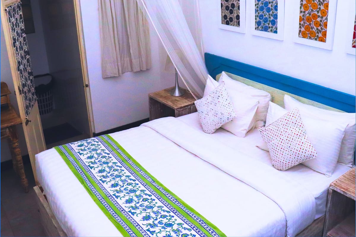Een slaapkamer met een bed, nachtkastje, deur en gordijn.