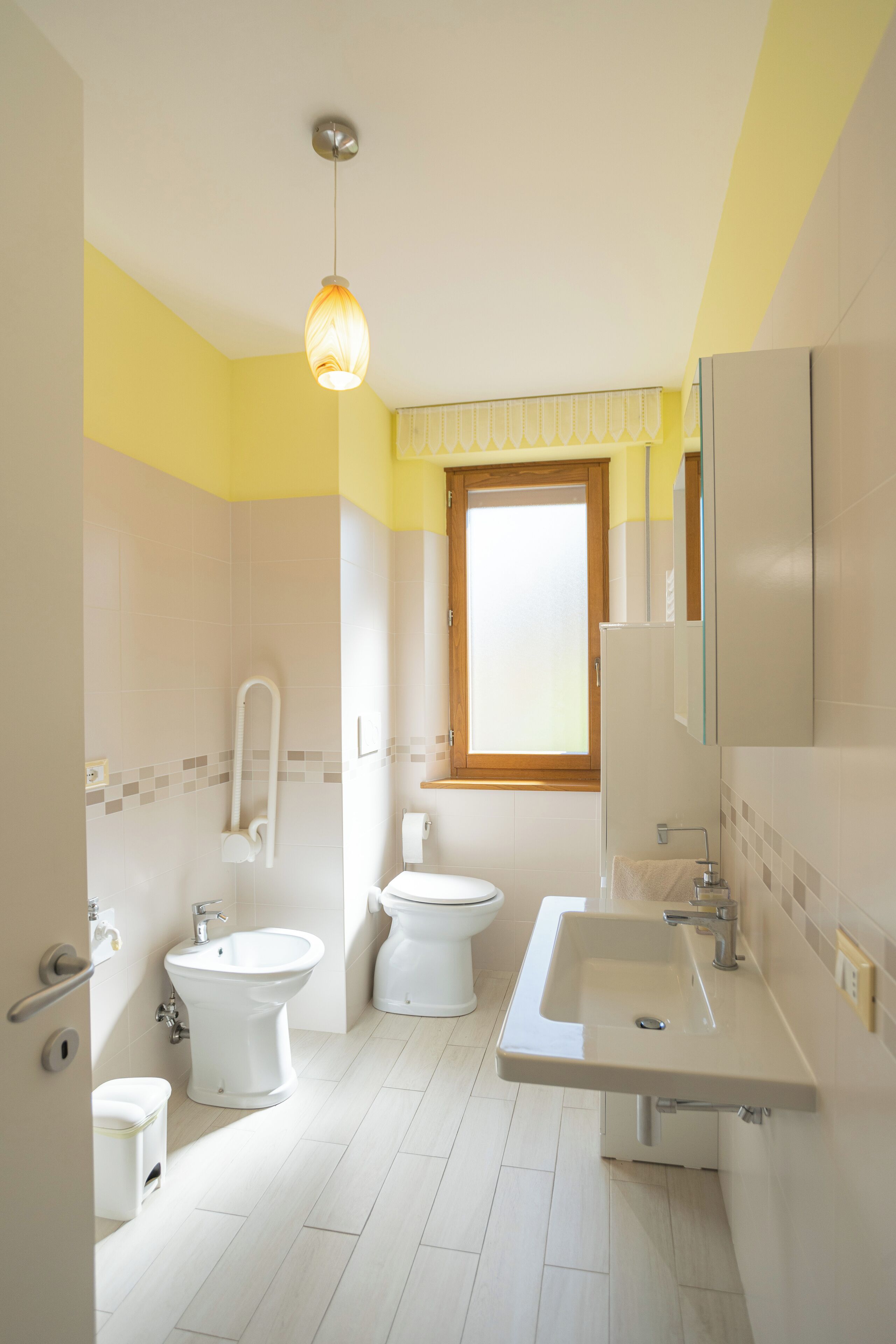 A bathroom with a toilet, bidet, sink, and a window.