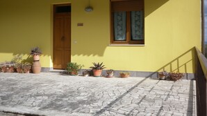 A yellow building with a wooden door, a window with curtains, and several potted plants on the ground. - Casa gli Ulivi: New cozy apartment, a few kilometers from Montepulciano.  (Montepulciano)