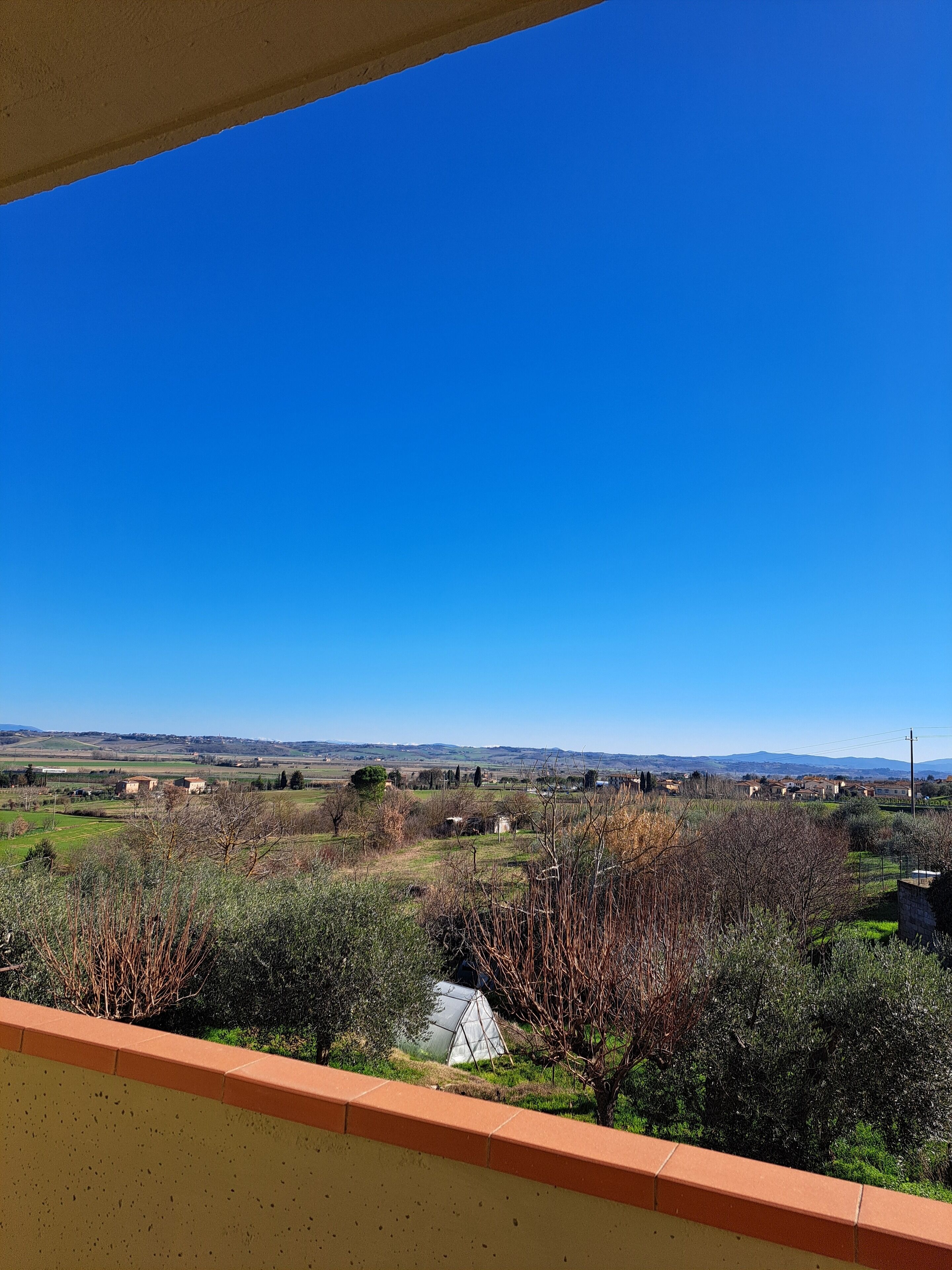 A balcony with a view of a rural landscape, including fields, trees, and distant hills.