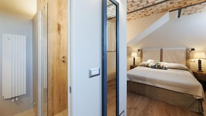 A bedroom with a sloped ceiling, a bed with a patterned pillow, bedside lamps, and a radiator.