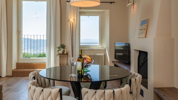 A dining area with a round table, four upholstered chairs, a hanging light fixture, a television, and a fireplace.