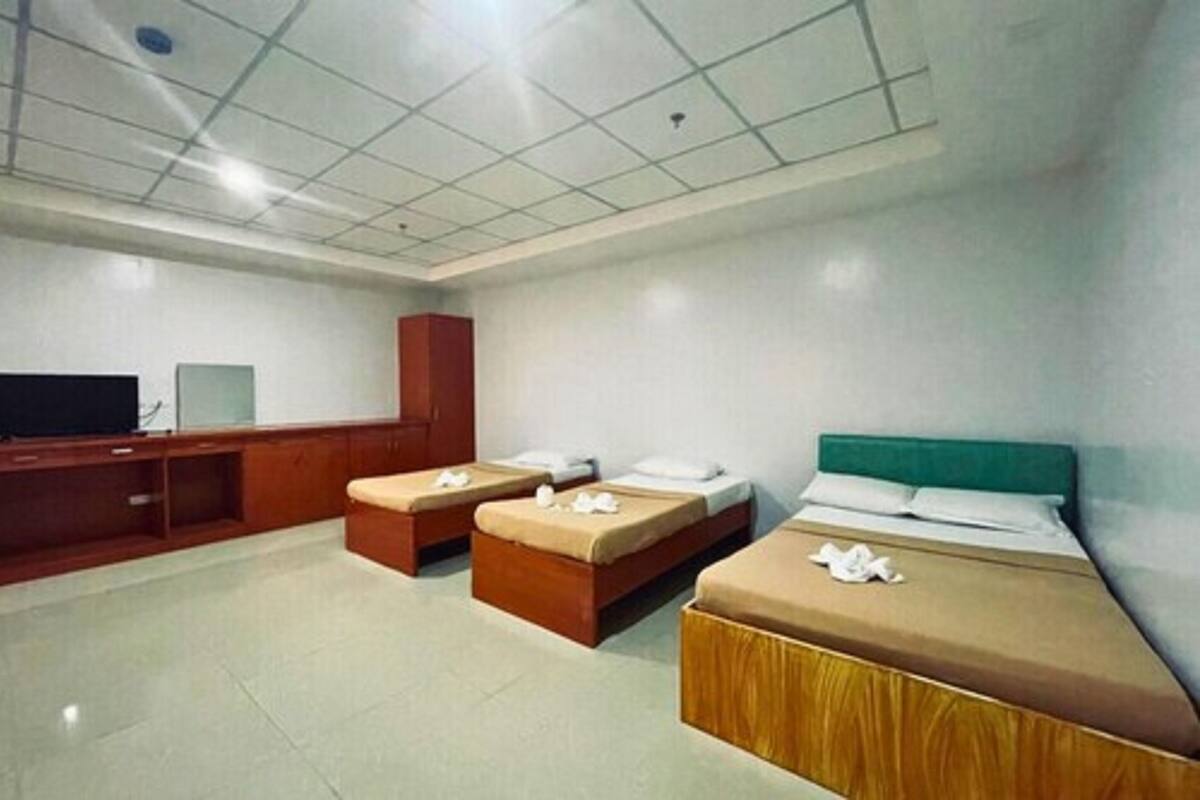 A hotel room with three beds, a television, and a wooden cabinet.