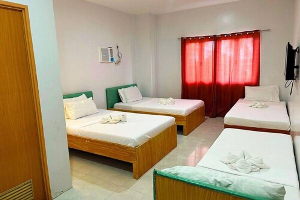 A hotel room with two single beds, a wooden door, a wall-mounted phone, and red curtains.