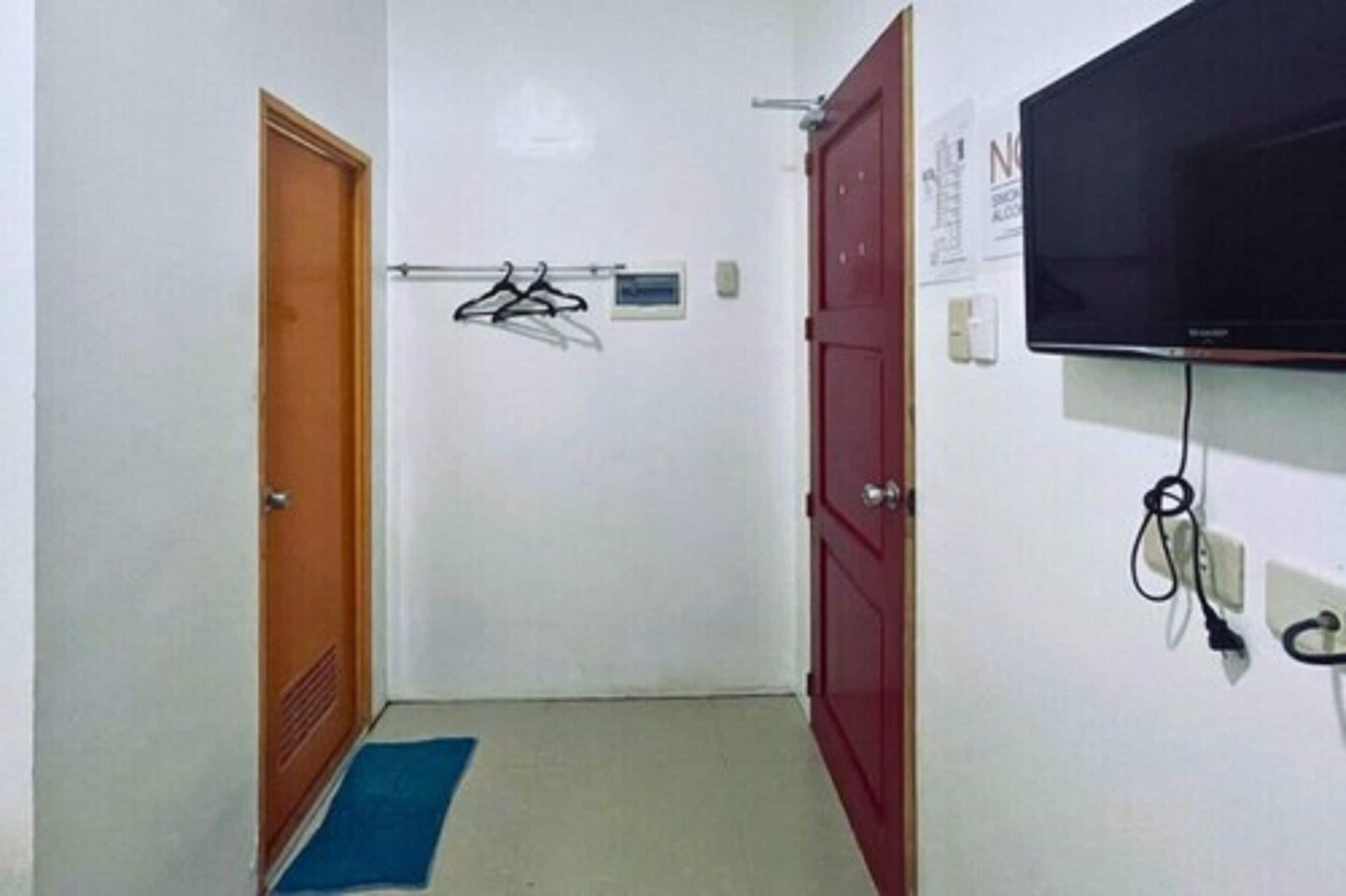 A hallway with a wooden door, a red door, a blue mat, a clothes rack, and a television mounted on the wall.