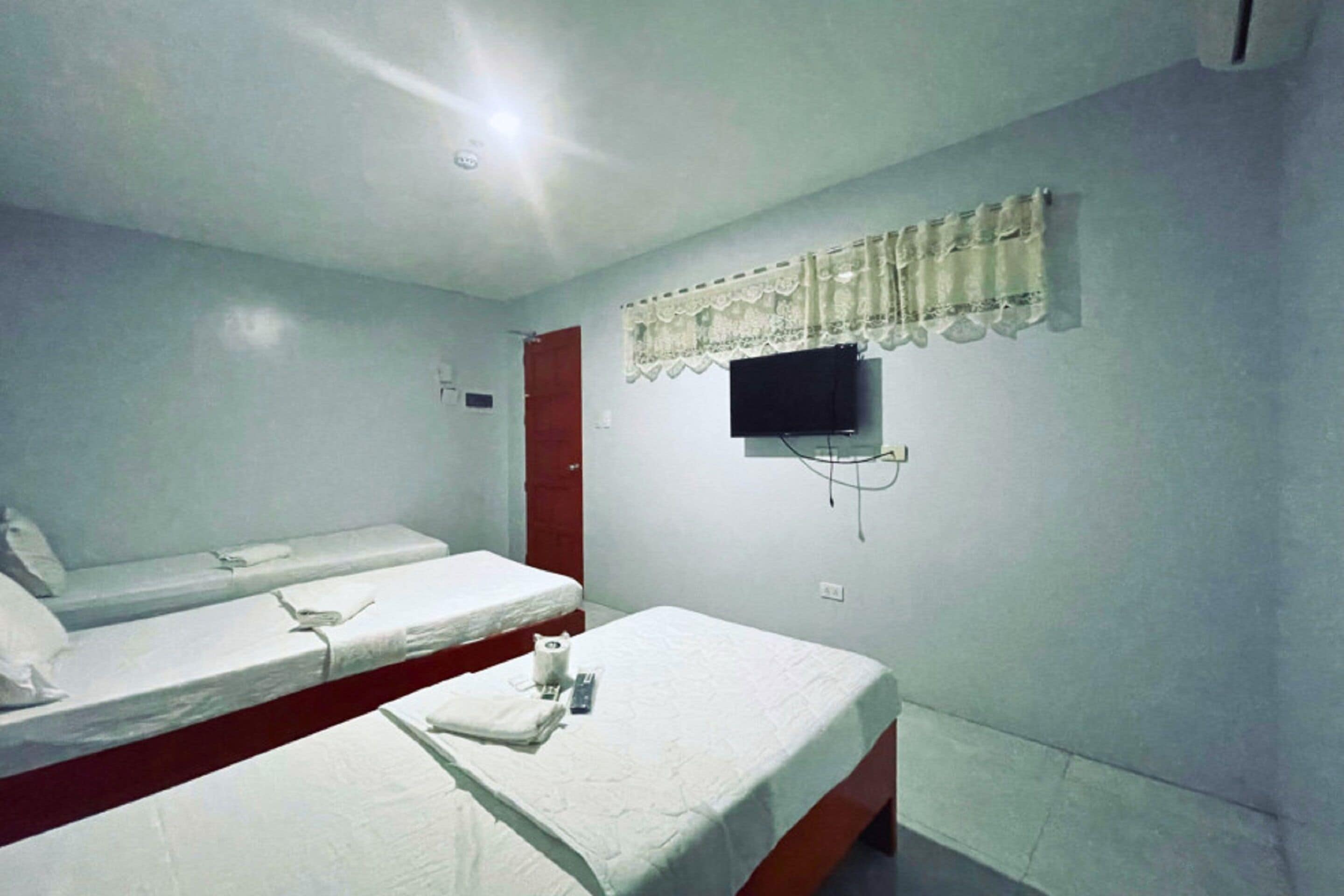 A room with two single beds, a television mounted on the wall, and a red door.