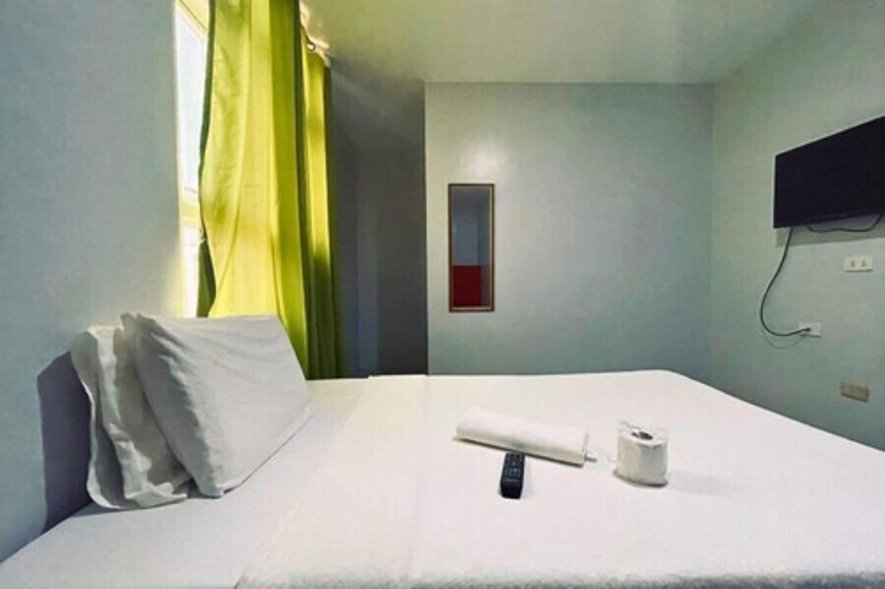 A hotel room with a bed, a remote control, and a toilet paper roll.