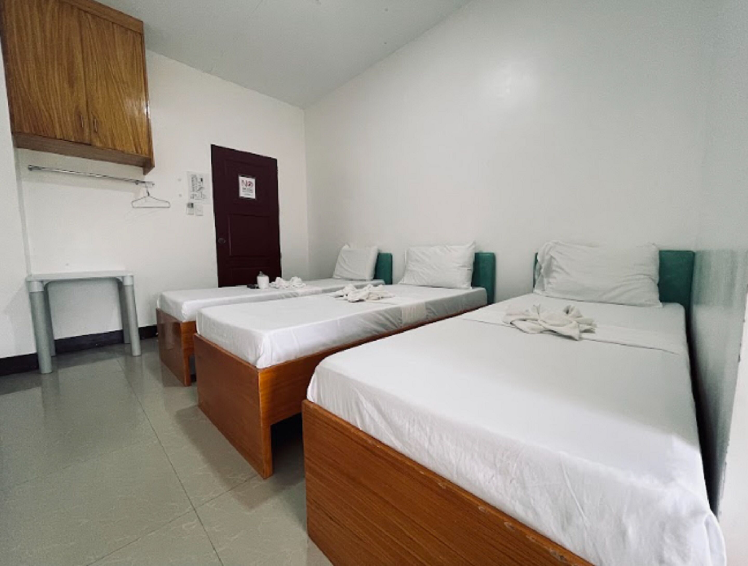 Habitación de hotel con dos camas individuales, un armario de madera, una mesita pequeña y una puerta con un cartel.