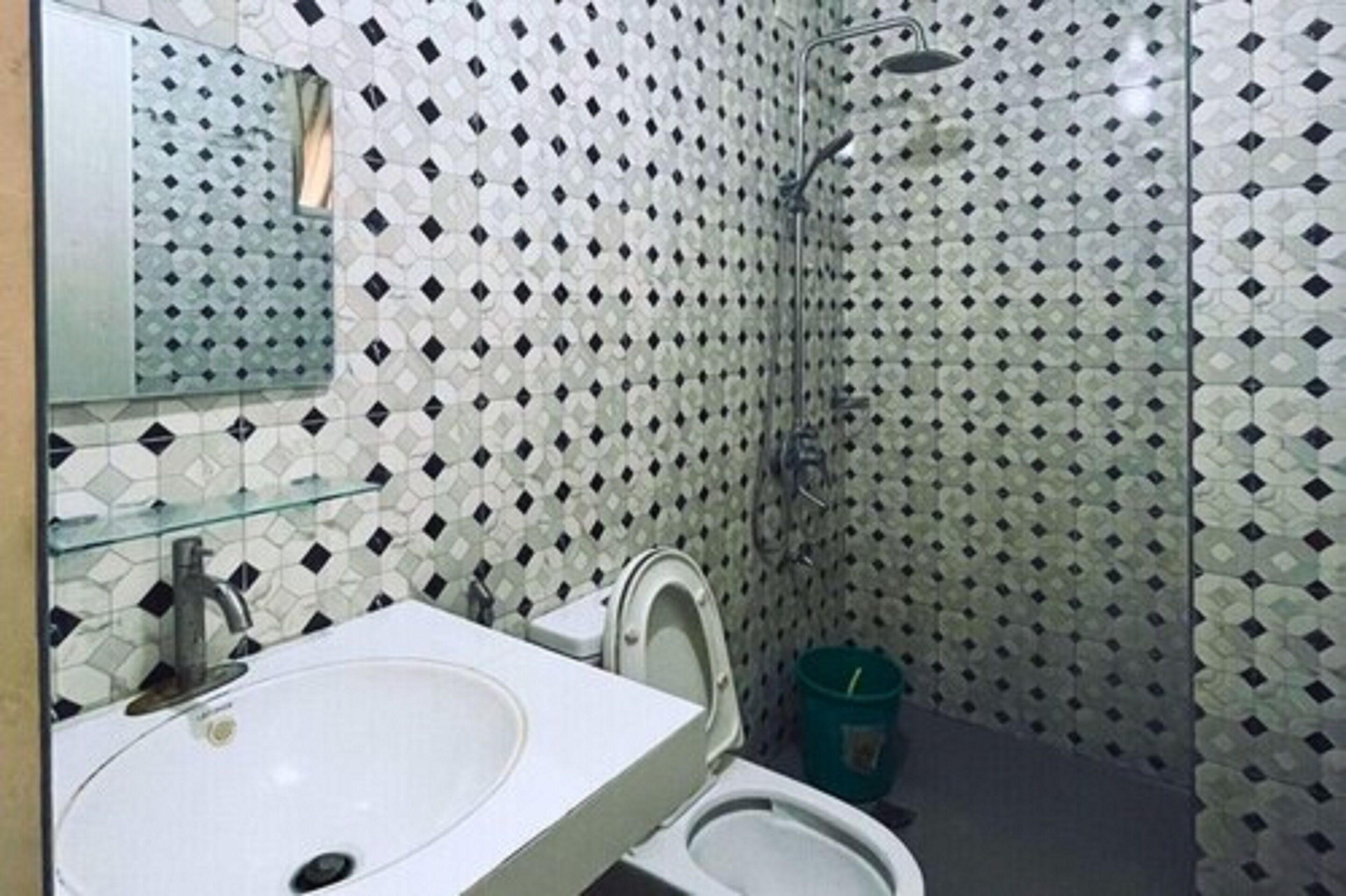 Un baño con lavamanos blanco, inodoro y ducha. Las paredes están cubiertas de azulejos con un diseño de rombos.