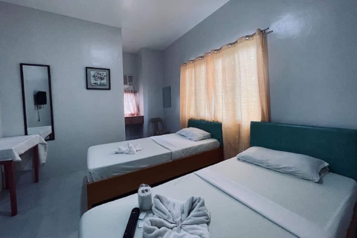 A hotel room with two single beds, a desk with a chair, a mirror, and a window with curtains.