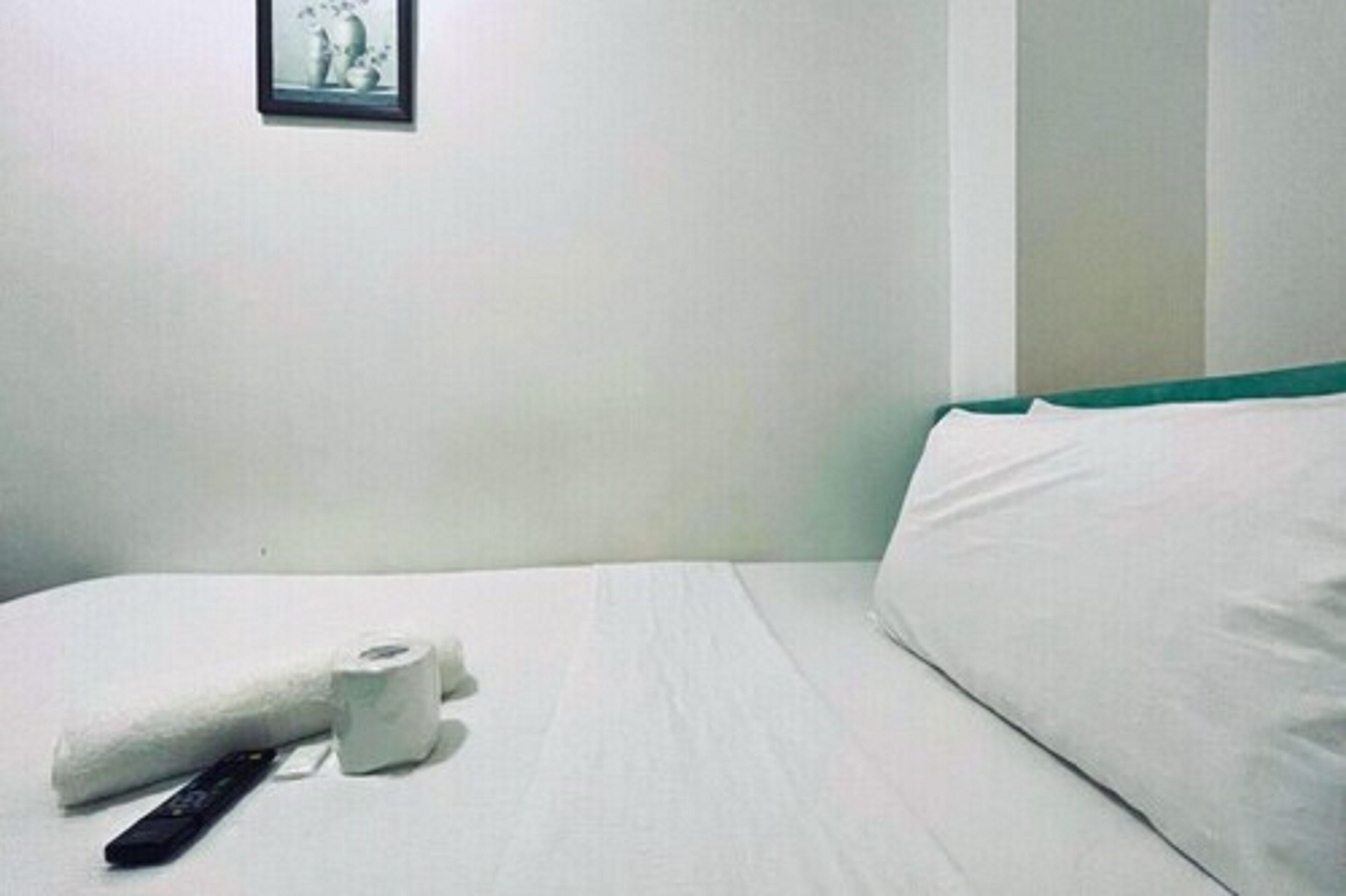 Een hotelkamer met een opgemaakt bed, een afstandsbediening en een rol toiletpapier op het bed.