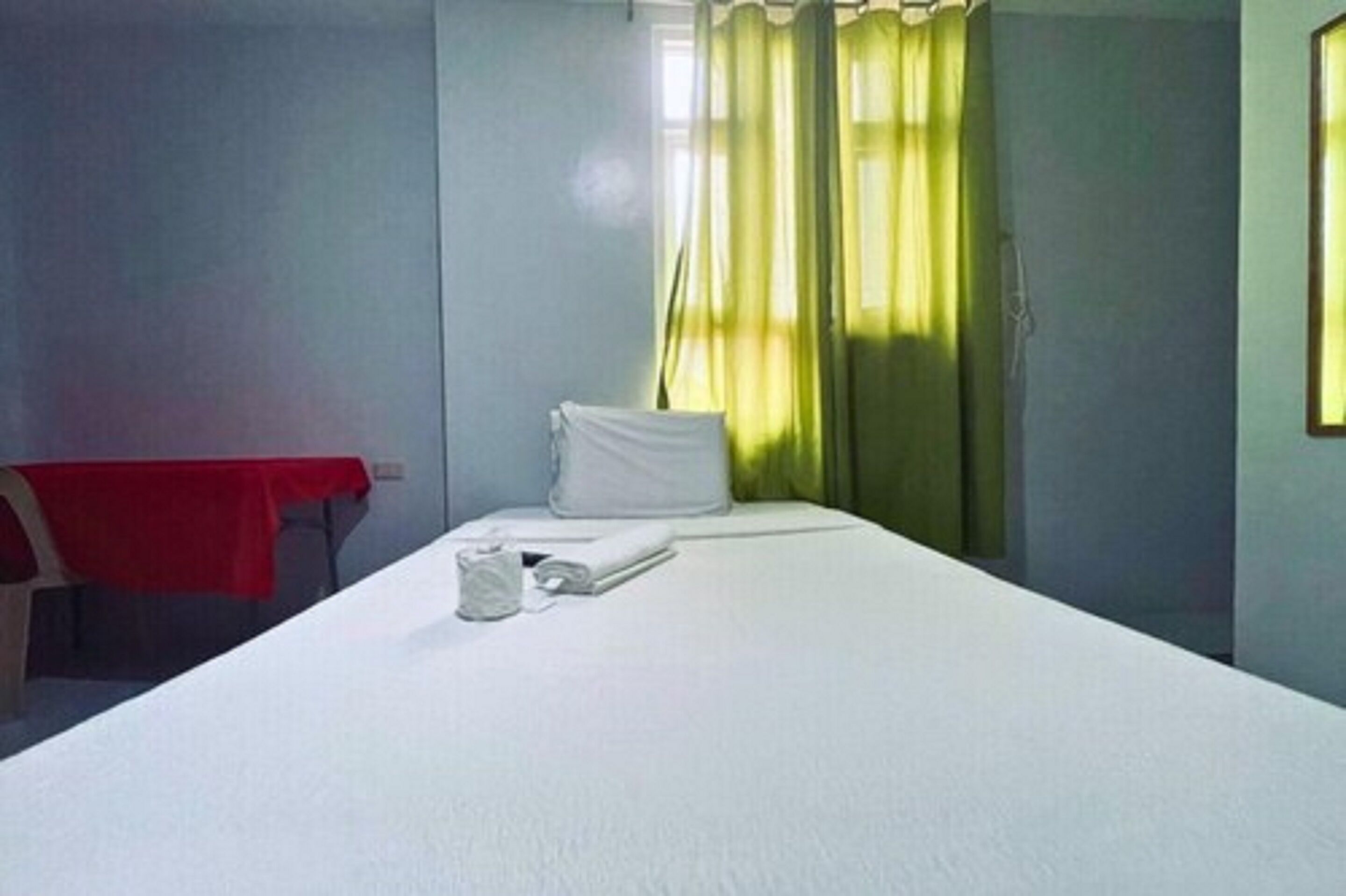 Una cama individual con sábanas blancas, mantel rojo y almohada.