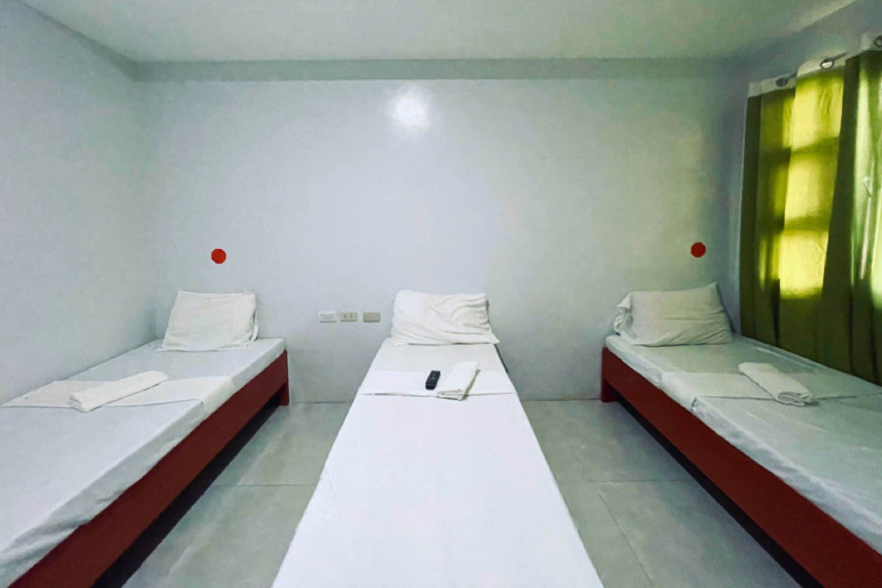 A room with three single beds aligned in a row, each with white bedding and red headboards.