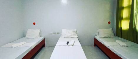 A room with three single beds aligned in a row, each with white bedding and red headboards.