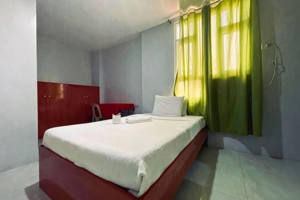 A single bed with a white mattress and pillows, a red wardrobe, and a shower curtain.
