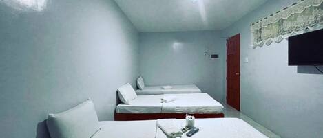 A small, clean room with three single beds, a TV mounted on the wall, and a simple, functional design.