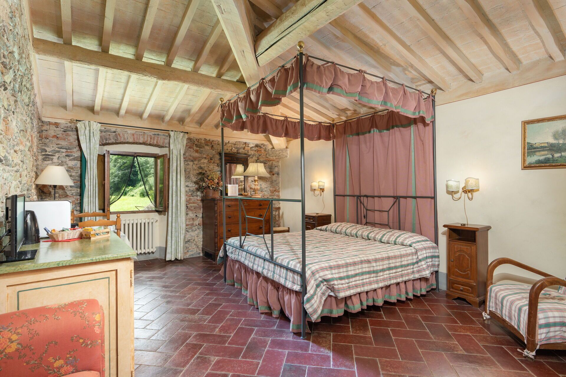 Un dormitorio con cama con dosel, un escritorio con lámpara, una pared de piedra y una ventana con cortinas.