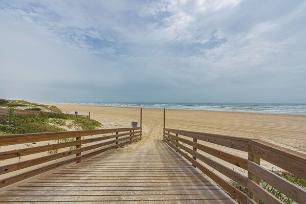 Une promenade en bois mène à une plage de sable, avec l’océan en toile de fond.