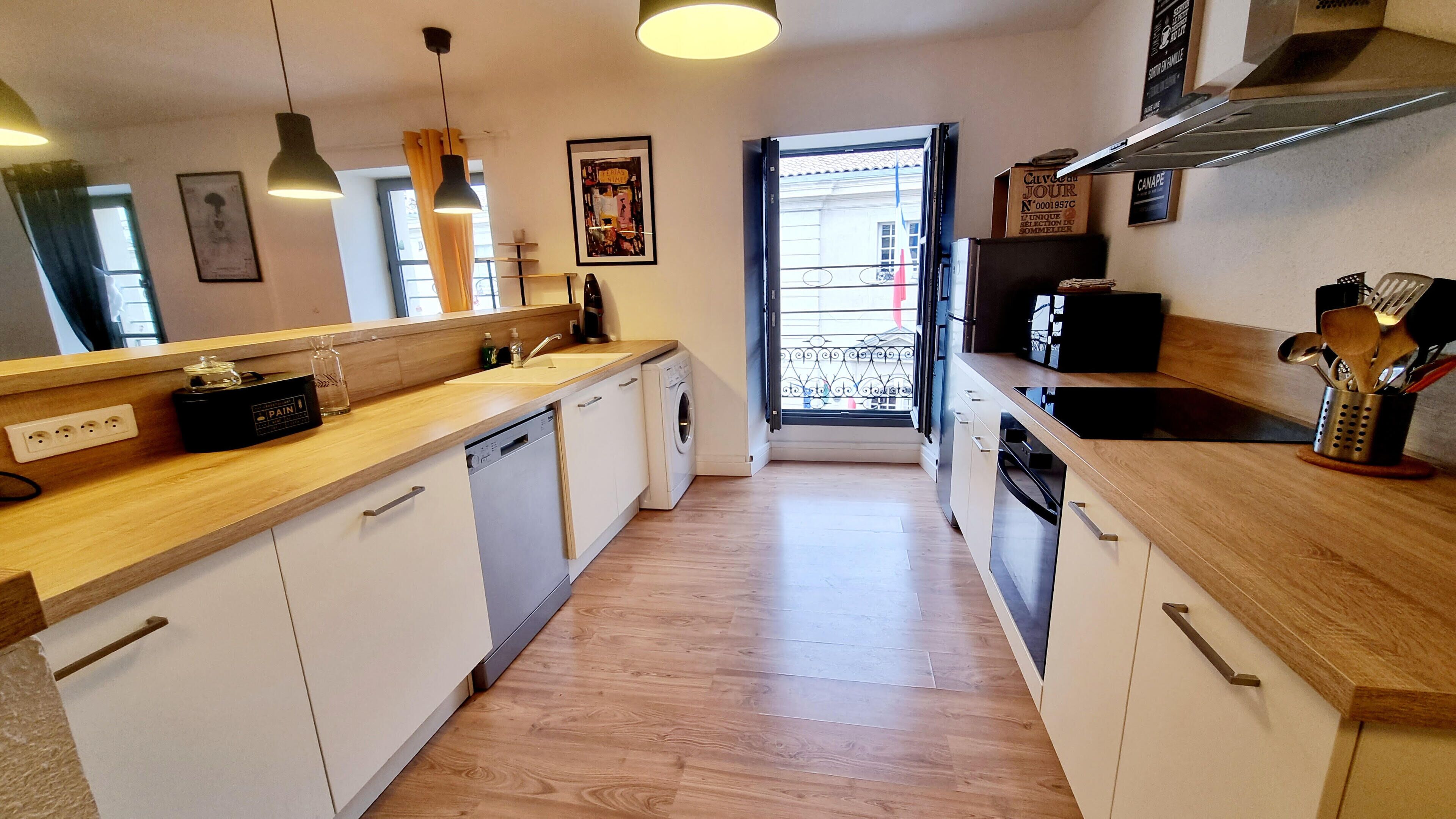 A modern kitchen with white cabinets, wooden countertops, a built-in dishwasher, and a window with a view of the street.