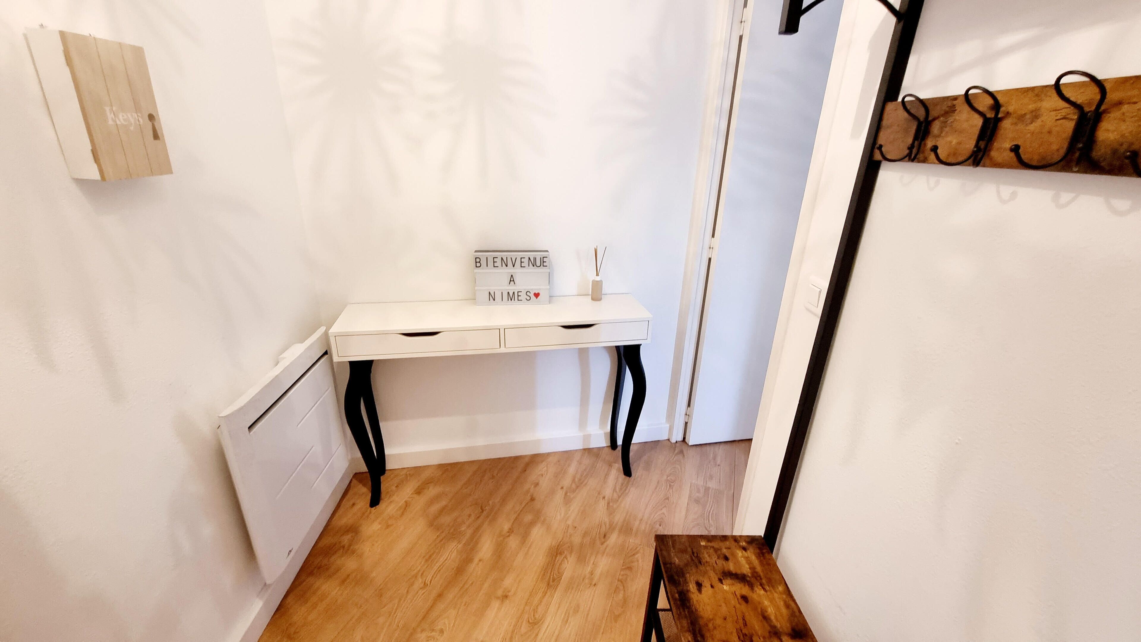 A small, white desk with a sign reading "BIENVENUE A NIMES" and a vase with reeds.