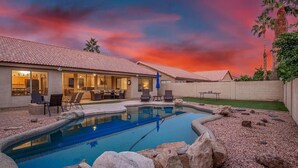 Quintal residencial com piscina, móveis de jardim e uma casa com telhado cerâmico.