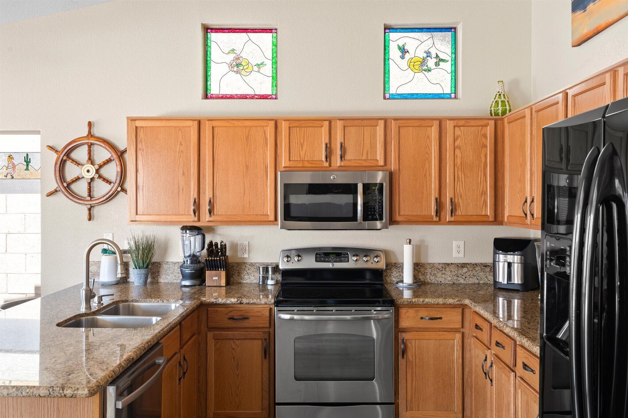 Una cocina con armarios de madera, electrodomésticos de acero inoxidable, encimera de granito y dos ventanas de vitral.