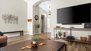 Uma sala de estar moderna com uma mesa de centro de madeira escura, uma grande TV de tela plana fixada na parede e um banco ao longo da parede.
