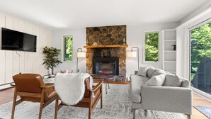 A living room with a stone fireplace, a flat-screen TV mounted on the wall, and a grey sofa. - The Overlook - Hot Tub, Game Room, 5min to MTN (Killington)