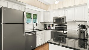 A modern kitchen with white cabinets, stainless steel appliances, and a black granite countertop. - The Overlook - Hot Tub, Game Room, 5min to MTN (Killington)