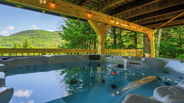 A hot tub with a wooden deck and a view of a forested hill. - The Overlook - Hot Tub, Game Room, 5min to MTN (Killington)
