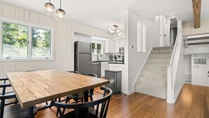 A modern kitchen with a wooden dining table, stainless steel appliances, and a staircase leading to an upper level. - The Overlook - Hot Tub, Game Room, 5min to MTN (Killington)