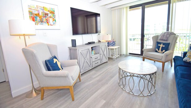 A modern living room with a flat-screen TV, a round coffee table, and two armchairs with decorative pillows. - Jada 2B-Oceanside 77th St, Free WiFi, Pool, Elev, W/D, AC (Ocean City)