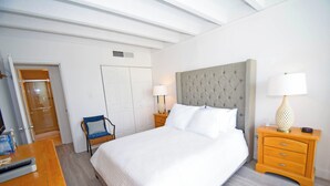 A neatly arranged bedroom with a large bed, a chair, a wooden nightstand with a lamp, and a wardrobe. - Jada 2B-Oceanside 77th St, Free WiFi, Pool, Elev, W/D, AC (Ocean City)