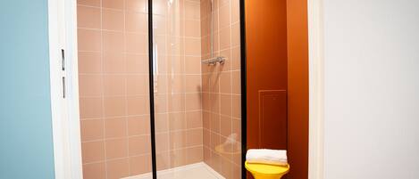 Um chuveiro com porta de vidro, vaso sanitário amarelo e pia branca.