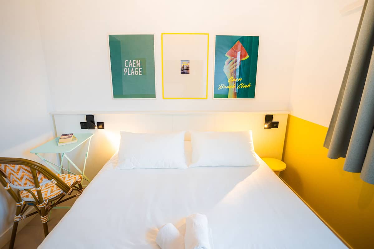 Ein Hotelzimmer mit einem Bett, einem kleinen Tisch mit Stuhl und Wandbildern.