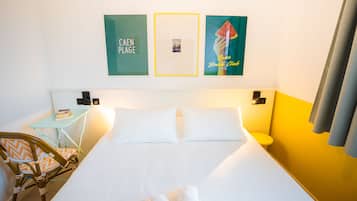 Une chambre d’hôtel avec un lit, une petite table et une chaise, ainsi que des œuvres d’art accrochées au mur.