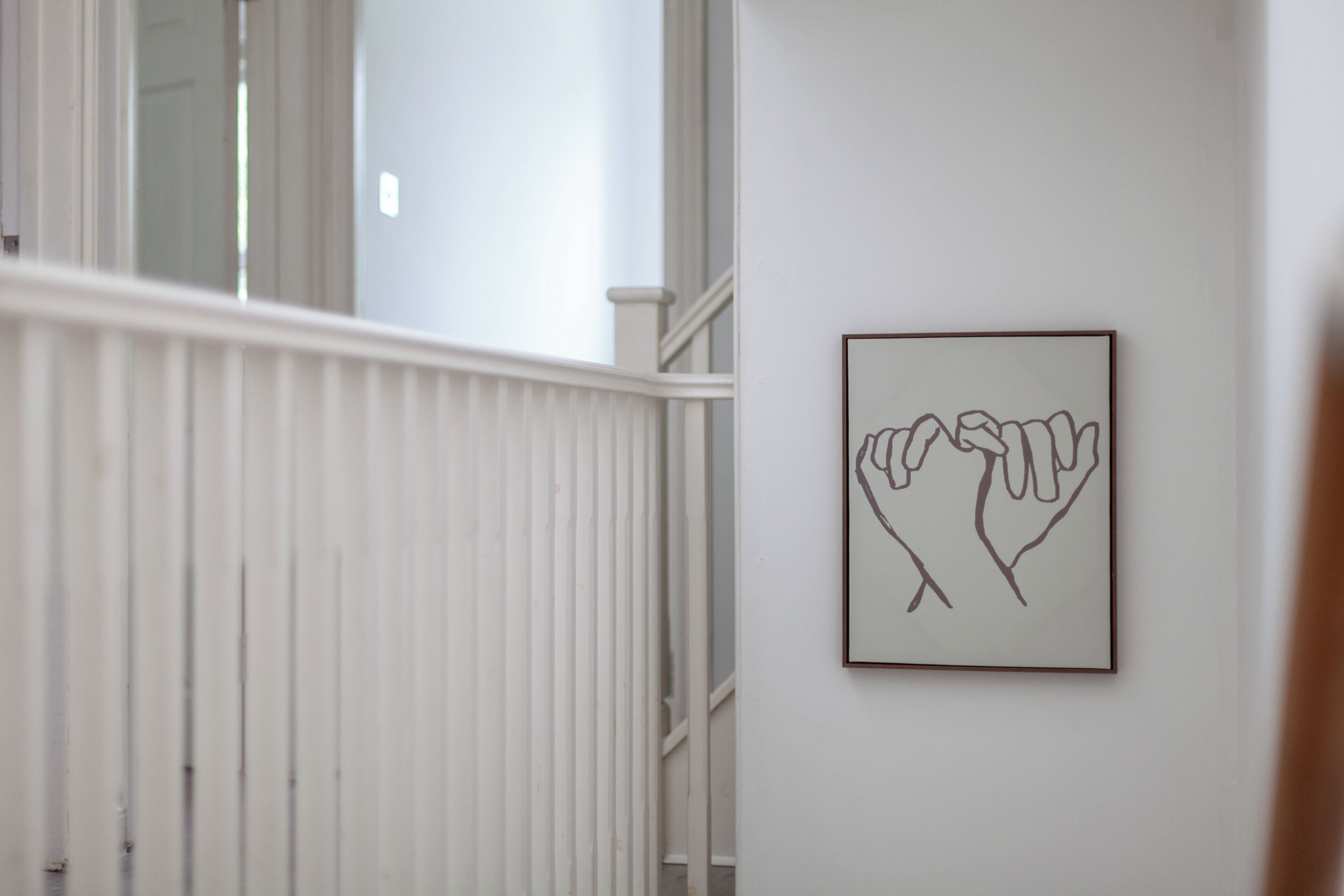 A staircase with white railings and a framed artwork of two hands on the wall.