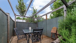 A wooden deck with a table and chairs, surrounded by a wooden fence and greenery. - The Harlesden Villas (London)