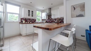A modern kitchen with white cabinets, a wooden island, and bar stools. - The Harlesden Villas (London)