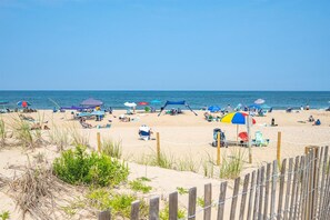 Une plage avec de nombreux parasols et des chaises de plage, une zone sablonneuse et une clôture en bois au premier plan.