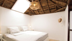 Een slaapkamer met een houten plafond, een bed met wit beddengoed, een nachtkastje met een lamp, en een vloerlamp.