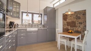 Een moderne keuken met grijze kastjes, een houten eettafel en een accentmuur van steen.
